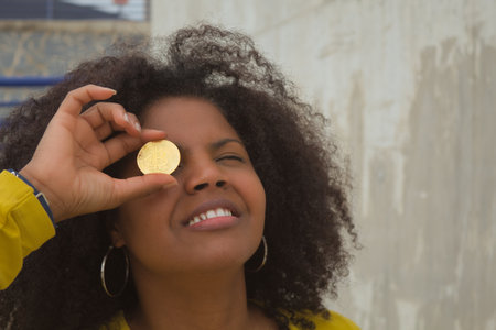 African american woman with afro hair and yellow t-shirt playing with cryptocurrencies in the foreground.の写真素材