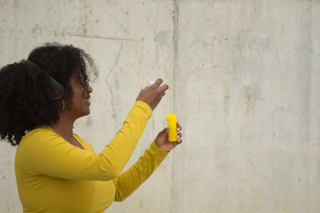 African american woman with afro hair and yellow t-shirt blowing soap bubbles on a concrete wall background.の写真素材