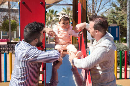 Gay married couple playing with their daughter at the playground very happy. Family diversity.の写真素材