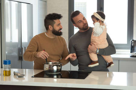 Gay married couple cooking with their daughter in the kitchen of their home. Family diversity.の写真素材