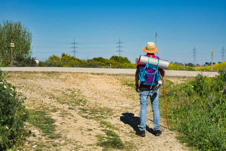 Pilgrim walking the road to Santiago with backpack, walking stick and hat. On a sunny day.の写真素材
