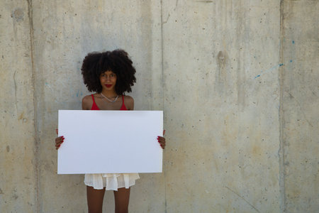 Young, beautiful African-American woman with a white banner on a gray cement background.の写真素材