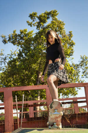 Young and beautiful girl with punk style and heterochromia concentrated to throw herself down a ramp with her feet on a skateboard. Vertical position.の写真素材