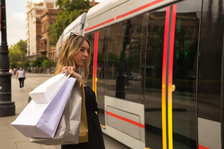 Young woman watching the subway pass by with shopping bags on her shoulder.の写真素材