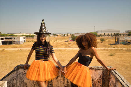 Young Hispanic and Latina women holding hands and leaning against a stone wall dressed for Halloween outside.の写真素材