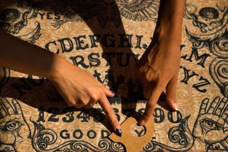 Detail of young Hispanic and Latina women's hands on a Ouija board signaling goodbye.の写真素材