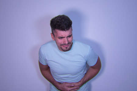 Young Hispanic male with hands on belly and stomach pain gesture on white background.の写真素材