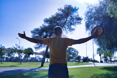 Hispanic mature adult man with a hat in his hand and open arms looking at the sun.の写真素材