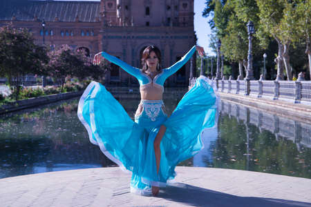 Middle-aged Hispanic woman in turquoise dress with rhinestones, raising her dress while belly dancing. Belly dance concept.の写真素材