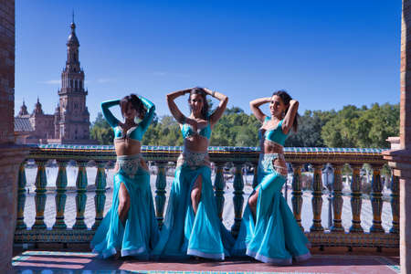 Three middle-aged Hispanic women, wearing turquoise dresses and rhinestones, to belly dance, posing next to a tiled railing. Belly dance concept.の写真素材