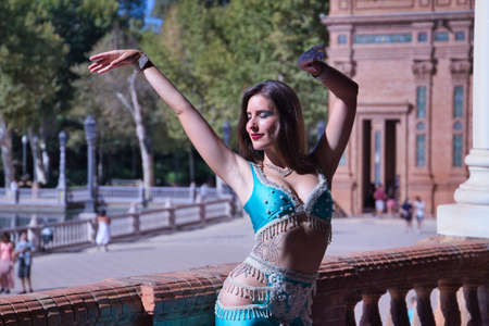 Middle-aged Hispanic woman, wearing turquoise costume and rhinestones, to dance belly dance, making figures while dancing next to a stone balustrade. Belly dance concept.の写真素材