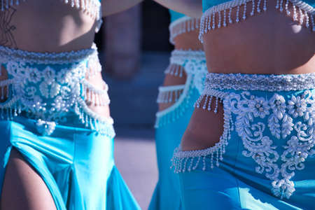 Detail of waists of three middle-aged Hispanic women, wearing turquoise costumes and rhinestones, to dance belly dance. Belly dance concept.の写真素材