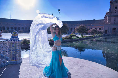 Middle-aged Hispanic woman in turquoise dress with rhinestones, belly dancing with a white veil. Belly dance concept.の写真素材