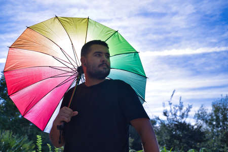 Portrait of gay boy with open backlit rainbow umbrella over shoulder. Concept gay, lgbtq +, inclusion, lesbian, lgbtq.の写真素材