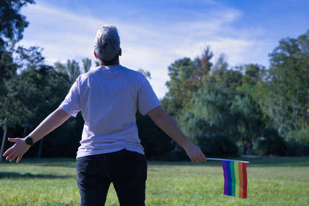 Non-binary person, back turned, arms outstretched, holding gay pride flag. Non-binary concept, lgbtq +, inclusion, gay, lesbian, lgbtq.の写真素材