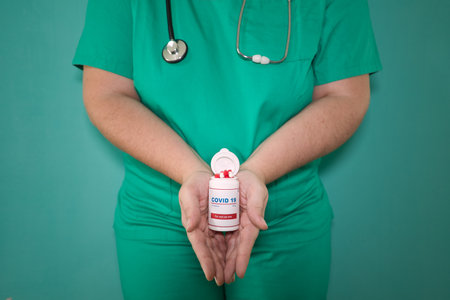 Doctor in green scrubs and stethoscope holding a bottle of antiviral pills against the Covid 19 virus. Pandemic concept, treatment, capsules, pills.の写真素材