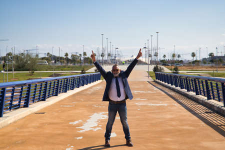Mature man, executive, gray haired, with beard, sunglasses, jacket and tie, with open arms, happy because business is going well for him. Concept executive, businessman, business, employment, triumph.の写真素材