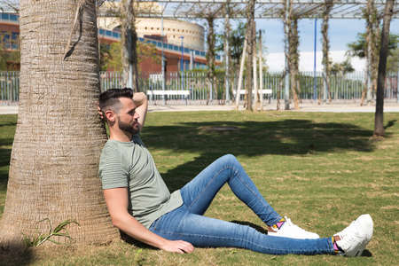 Young and handsome gay man, with a beard and green shirt, with blue eyes, perfect smile and waving a gay pride flag, smiling. Concept of gay pride, homosexual, lgtbi, pride day.の写真素材