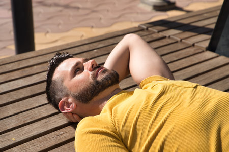 Portrait of handsome young man, with blue eyes and wearing yellow t-shirt, lying on a wooden slatted surface with thoughtful gesture. Concept beauty, fashion, thought, trend.の写真素材