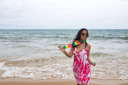 Young and beautiful South American woman, brunette, with sunglasses, bikini and flower necklace with a glass of blue wine in her hand, very happy and smiling. Summer concept, beach, drinks.の写真素材