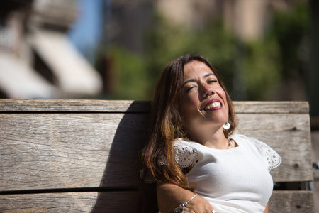 Woman with disability, reduced mobility and small stature sitting on a wooden bench, happy and relaxed sunbathing. Concept handicap, disability, incapacity, special needs, overcoming.の写真素材