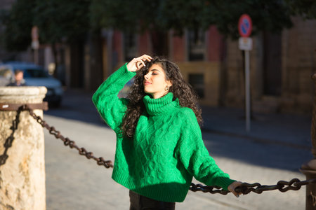 Young, beautiful, brunette woman with curly hair and a green turtleneck sweater, touching her hair with sensual and flirtatious attitude. Concept beauty, fashion, autumn, winter, cold, sensuality.の写真素材