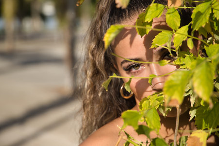 Portrait of Latin and Hispanic girl, young and beautiful, with beautiful green eyes and big eyelashes, looking through green leaves. Concept beauty, looks, eyes, nature, green.の写真素材
