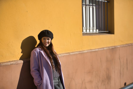 Young woman, beautiful, straight brown hair, sweater, coat and black beret, leaning against a wall, dreamy and thoughtful. Concept beauty, fashion, autumn, winter, cold.の写真素材