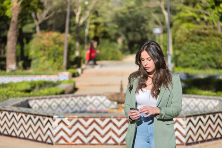 Young, pretty, Hispanic woman, brown hair, wearing a green jacket and jeans, looking at her sunglasses in an absent and thoughtful attitude. Concept beauty, fashion, thoughts, doubts.の写真素材