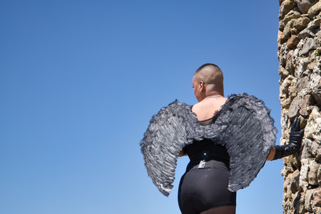 Non-binary person, young and South American, with black wings and leather gloves, bodice and black stockings, back, posing next to the keep of a medieval castle. Queen of the concept, lgbtq+, pride.の写真素材