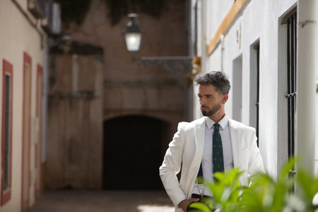 Attractive young businessman with beard, suit and tie, posing with hands in pockets behind green plants. Concept beauty, fashion, success, achiever, trend.の写真素材