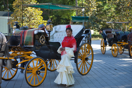 Young black and South American woman wearing a beige gypsy flamenco suit and red shawl, posing next to typical horse-drawn carriages of the city of Seville in Spain. Concept dance, folklore, art.の写真素材