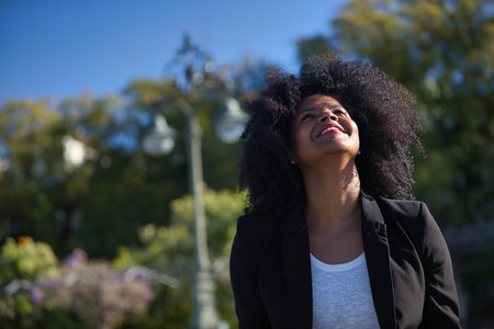 Portrait of young, beautiful, black woman with afro hair, wearing jacket, looking at the sky, grateful, praying. Concept gratitude, praying, current, modern.の写真素材
