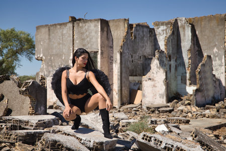 South American woman, young, beautiful, brunette with lingerie and black wings, posing crouched in the middle of the ruins of a building. Concept angels, beauty, costumes, wings, halloween.の写真素材