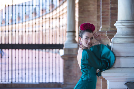 Young, beautiful, blonde woman in typical green colored flamenco suit, posing leaning on a marble column. Flamenco concept, typical Spanish, Seville, Andalusia.の写真素材