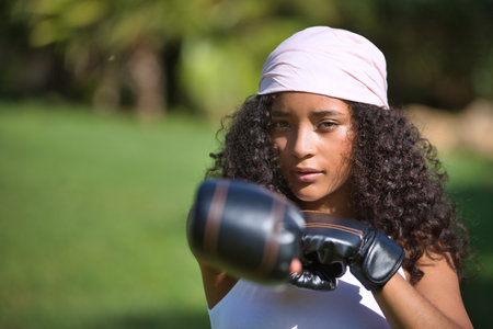 Portrait of Latina woman, young, beautiful, brunette, with curly hair, boxing gloves and a pink scarf of the fight against cancer on her head, depicting the fight against the disease.の写真素材