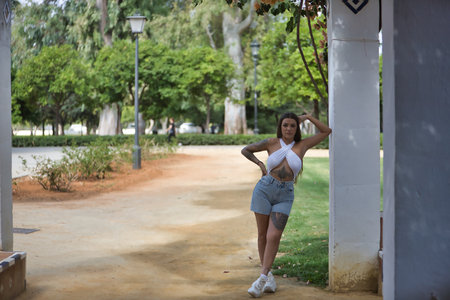 Young woman, brunette, beautiful, very tattooed, with white top and jeans, with serious and defiant look leaning on a column. Concept tattoos, nonconformism, rebel, trend, fashion.の写真素材