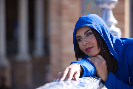 Portrait of Moroccan woman, young, beautiful, brunette, with blue abaya, with hood on, with sweet and dreamy look leaning on a beautiful tiled railing. Concept ethnicity, diversity, femininity, beautyの写真素材