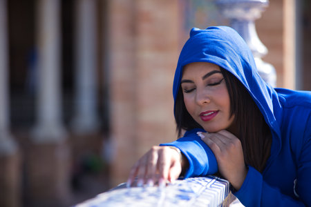 Portrait of Moroccan woman, young, beautiful, brunette, with blue abaya, hood on, eyes closed, leaning on a beautiful tiled railing. Concept ethnicity, diversity, femininity, beauty.の写真素材