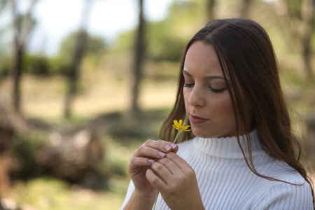 Beautiful young woman in white sweater, smelling a daisy in the middle of nature. Concept beauty, fashion, flowers, femininity.の写真素材