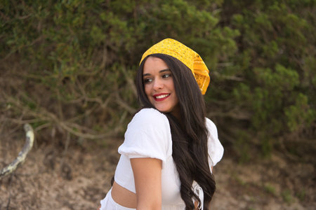 Portrait of a young, pretty woman, with black hair, wearing a white shirt, jeans and a yellow scarf on her head, with a sweet and tender look. Concept beauty, fashion, looks, tenderness, nature.の写真素材