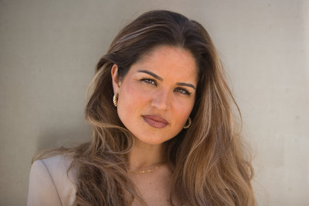 Close-up portrait of a young, beautiful, brown-haired woman in a light gray jacket suit, posing looking at the camera, on a gray metallic background.の写真素材