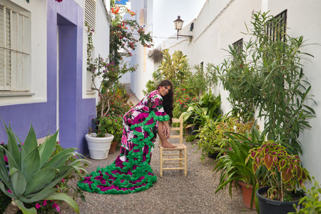 Young, pretty, brunette, flamenco dancer, showing her beautiful dress, posing with one foot on a chair, inside a nice, typical Andalusian courtyard full of flower pots.の写真素材