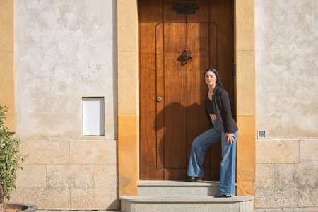 Young woman, brunette, blue eyes, Hispanic, wearing a black jacket and top, jeans, posing looking at the camera, leaning against the frame of a door. Concept: model, beauty, fashion.の写真素材