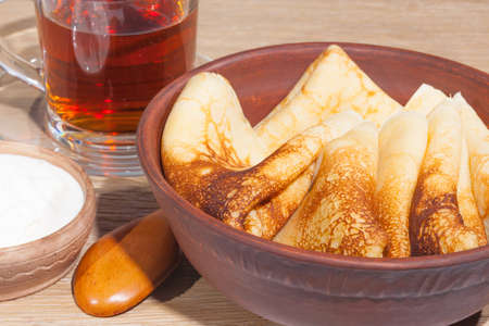 traditional oiled food in vintage style: pancakes with sour cream in and a clay plate and tea in a glass cup with a wooden spoon on an oak table
の写真素材