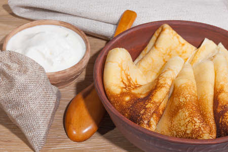 traditional oily food in vintage style: pancakes with sour cream in and a clay dish with a wooden spoon on an oak tableの写真素材