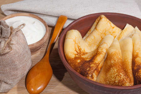 traditional oily food in vintage style: pancakes with sour cream in and a clay dish with a wooden spoon on an oak tableの写真素材