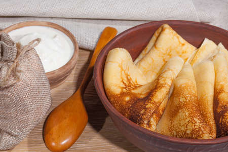 traditional oily food in vintage style: pancakes with sour cream in and a clay dish with a wooden spoon on an oak tableの写真素材