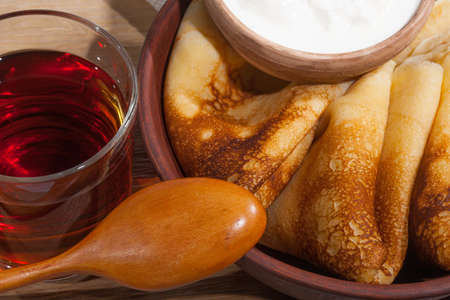 traditional oiled food in vintage style: pancakes with sour cream in and a clay plate and tea in a glass cup with a wooden spoon on an oak table
の写真素材