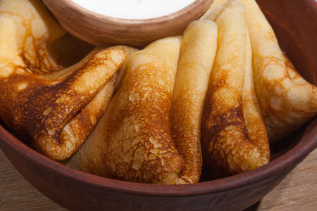 traditional oily food in vintage style: pancakes with sour cream in and a clay dish with a wooden spoon on an oak tableの写真素材
